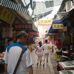 Larry, walking through a little market filled with random junk and unsanitary food.